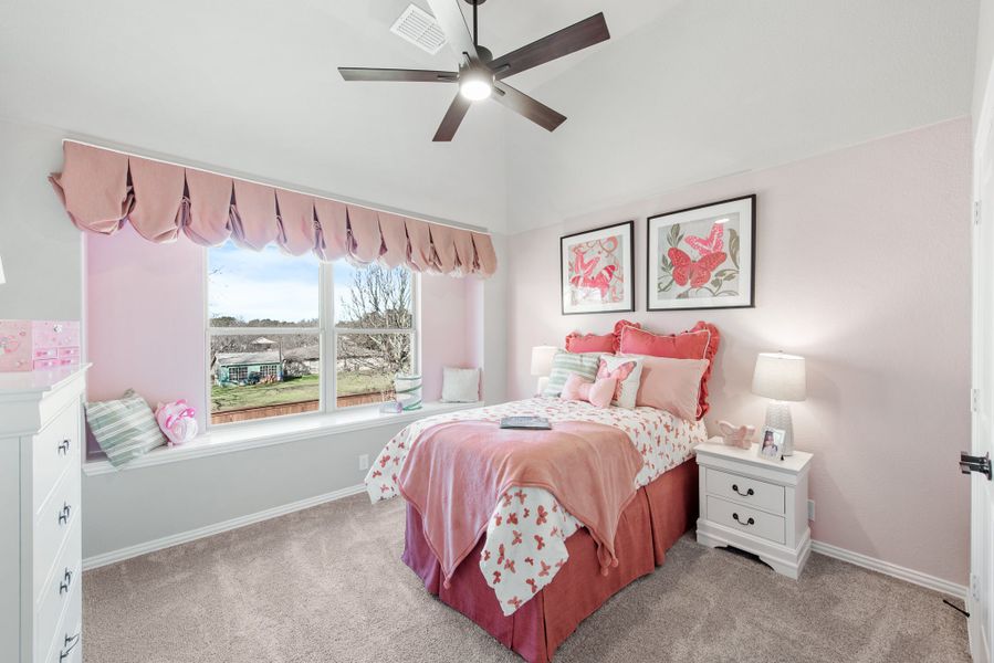 Children's bedroom with pink decor, ceiling fan, window seat, and carpet flooring