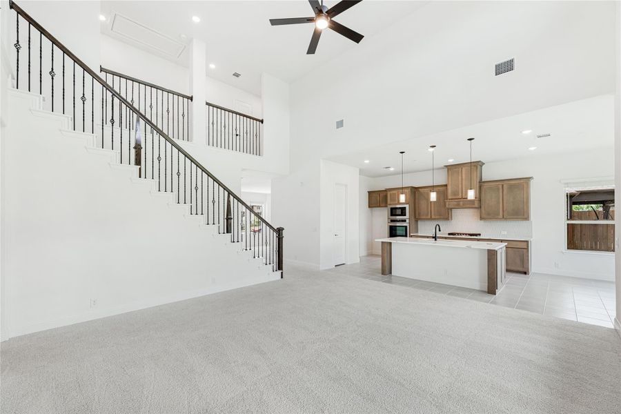 Open living area with high ceilings, staircase, and kitchen with wood cabinets and center island