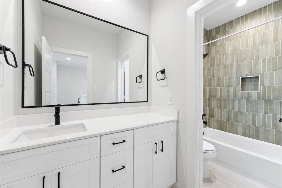 Ensuite bathroom featuring a quartz-topped vanity, matte black fixtures, and a tub-shower combo with warm vertical tile for a modern, spa-inspired finish.