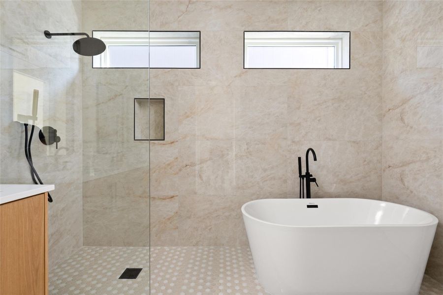 Fine stone tile surrounds a freestanding soaking tub and glass-enclosed shower with black hardware.