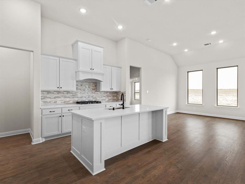 Kitchen with recessed lighting, white cabinets, a center island with sink, vaulted ceiling, and backsplash