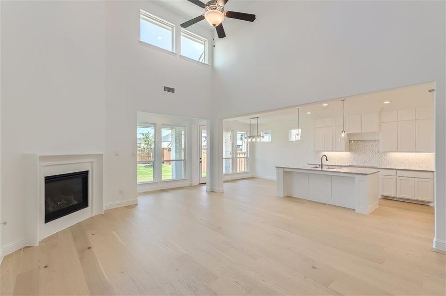 Unfurnished living room with light hardwood / wood-style floors, sink, a towering ceiling, and ceiling fan