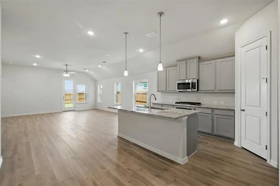 Kitchen with gray cabinets, light stone countertops, a center island with sink, open floor plan, and lofted ceiling