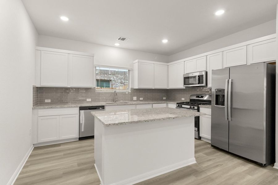 The kitchen features white cabinetry, stainless steel appliances, and a central island with a granite countertop