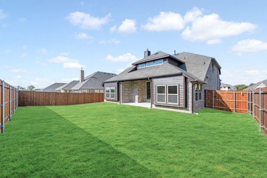Backyard of two-story brick home with large green lawn and wood privacy fence on both sides.