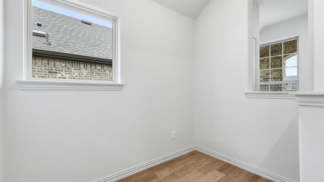 Recessed corner space featuring wood-finish flooring, crisp white walls, and a large window with white trim
