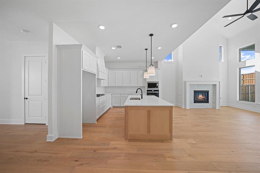 Kitchen featuring open floor plan, white cabinetry, decorative light fixtures, a glass covered fireplace, and a center island with sink