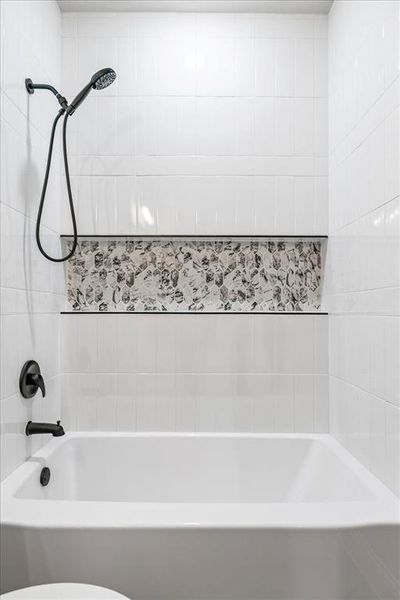 White subway tile surround with a pebble tile accent niche, complete with a matte black showerhead and tub faucet