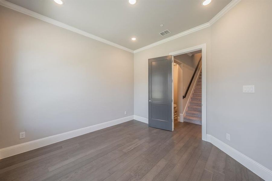 Recessed lighting illuminates this room featuring wood-finish flooring, white baseboards, and crown molding