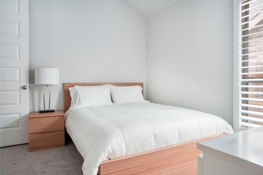This bedroom features a modern, minimalist design with a comfortable bed, neutral tones, and ample natural light from large windows. The space includes a wooden nightstand with a sleek lamp, creating a cozy and inviting atmosphere. This bedroom features a modern, minimalist design with a comfortable bed, neutral tones, and ample natural light from large windows. The space includes a wooden nightstand with a sleek lamp, creating a cozy and inviting atmosphere.
