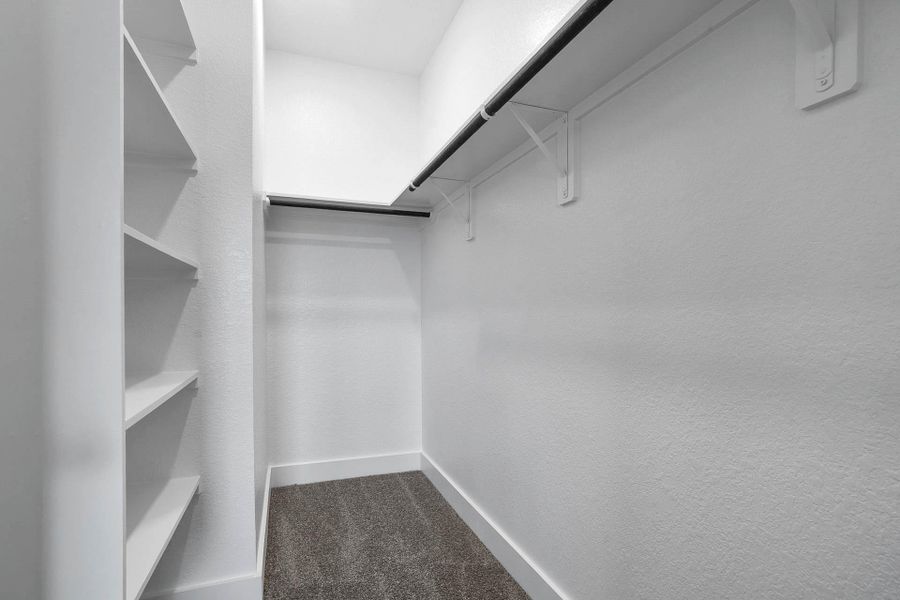 A spacious primary closet featuring built-in white shelving and ample hanging space, offering excellent organization potential for your wardrobe. A spacious primary closet featuring built-in white shelving and ample hanging space, offering excellent organization potential for your wardrobe.