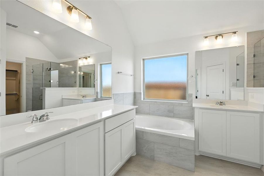 Bathroom with a stall shower, two vanities, vaulted ceiling, a walk in closet, and a garden tub