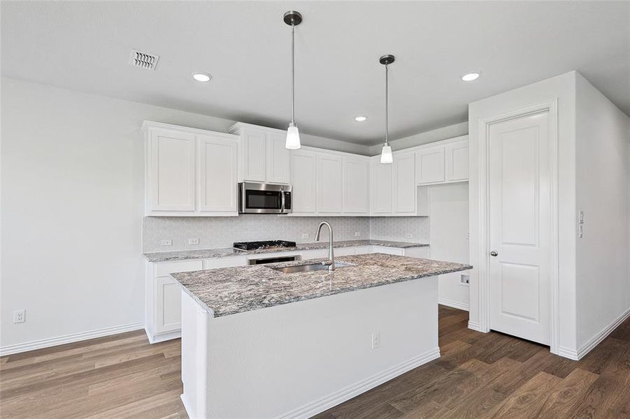 Kitchen with sink, a kitchen island with sink, white cabinets, and hardwood / wood-style floors