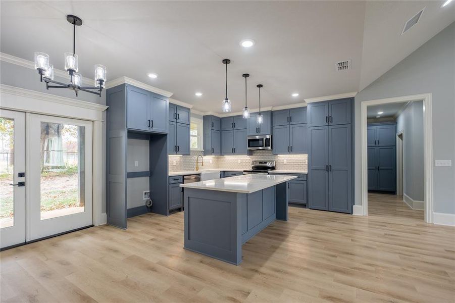 Kitchen with a kitchen island, decorative light fixtures, french doors, ornamental molding, and stainless steel appliances Kitchen with a kitchen island, decorative light fixtures, french doors, ornamental molding, and stainless steel appliances