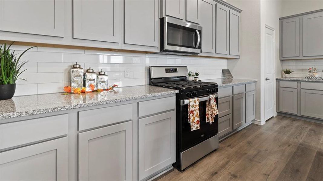 Kitchen featuring stainless steel appliances, gray cabinets, light stone counters, and decorative backsplash