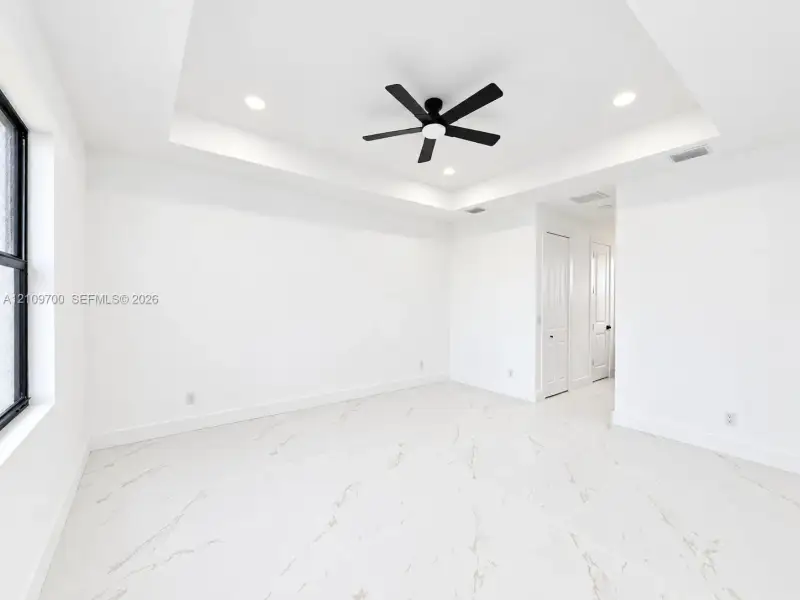 Tray ceiling featuring a central matte black ceiling fan, recessed lighting, and large-format tile flooring with marble-style veining