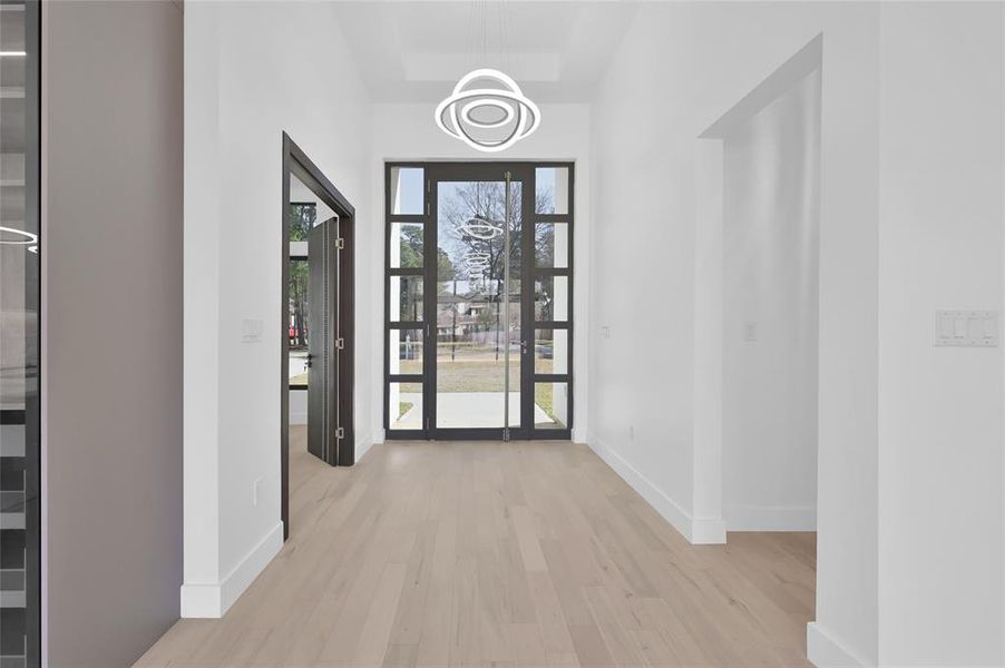 This photo showcases a modern entryway with light wood flooring and a large, stylish glass front door, allowing plenty of natural light. The space is open and bright, creating an inviting first impression.