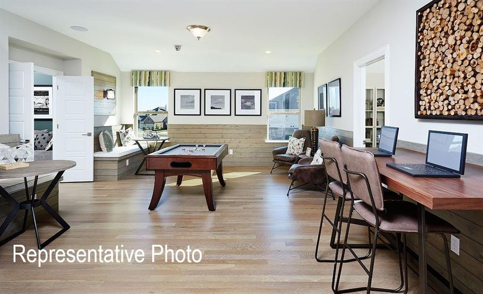 Spacious bonus room featuring wood-finish flooring, shiplap accent walls, multiple windows, built-in bench seating, and a dedicated desk area with built-in countertop Spacious bonus room featuring wood-finish flooring, shiplap accent walls, multiple windows, built-in bench seating, and a dedicated desk area with built-in countertop