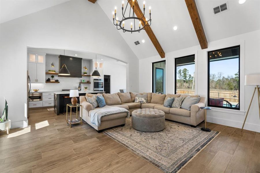 Living room with light wood-style flooring, visible vents, a chandelier, beamed ceiling, and high vaulted ceiling Living room with light wood-style flooring, visible vents, a chandelier, beamed ceiling, and high vaulted ceiling