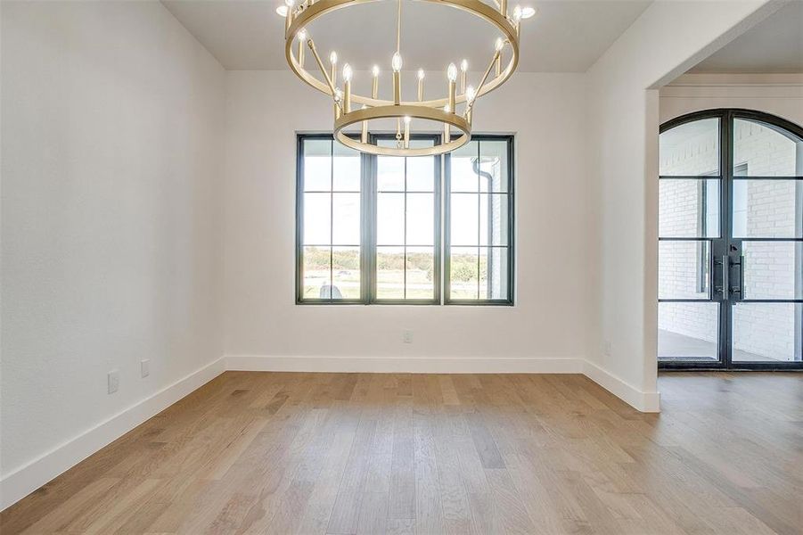 Unfurnished room featuring an inviting chandelier, light hardwood / wood-style flooring, and french doors