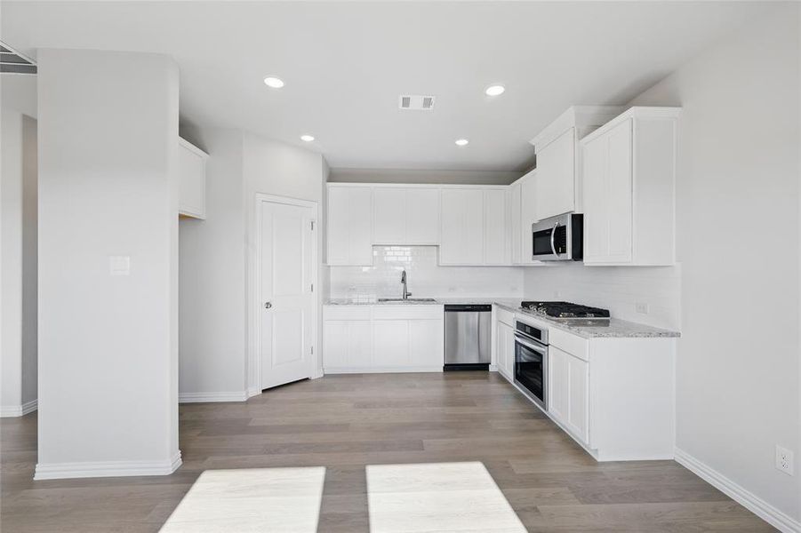 Kitchen with stainless steel appliances, backsplash, light wood finished floors, white cabinets, and recessed lighting Kitchen with stainless steel appliances, backsplash, light wood finished floors, white cabinets, and recessed lighting