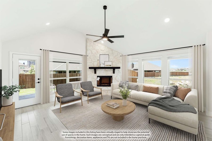 Living room with vaulted ceiling, stone fireplace, ceiling fan, and large windows with backyard views