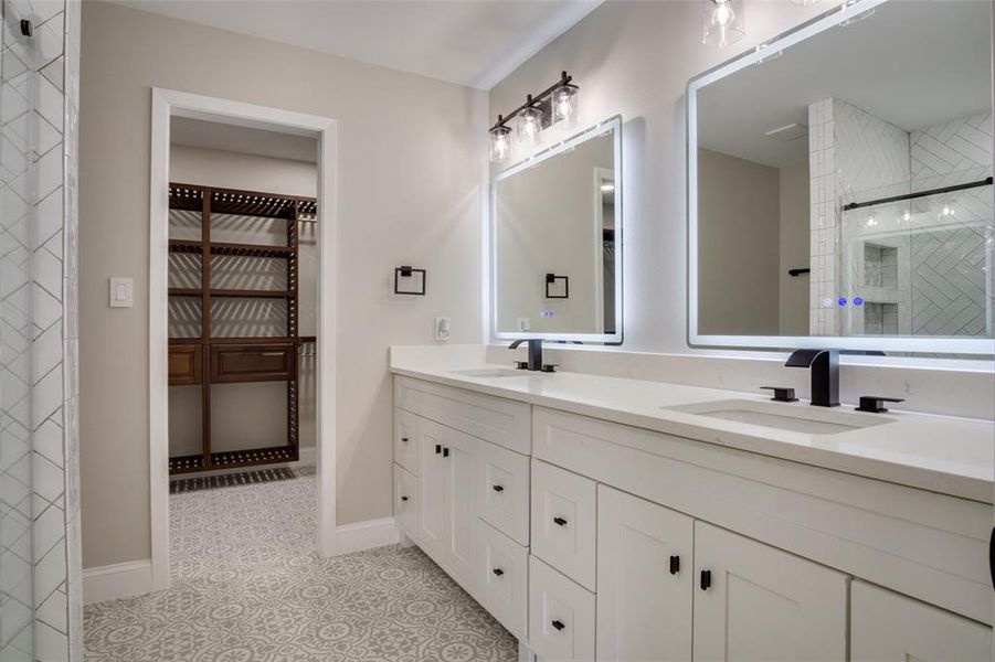 Bathroom featuring a walk in closet, double vanity, a tile shower, and a sink