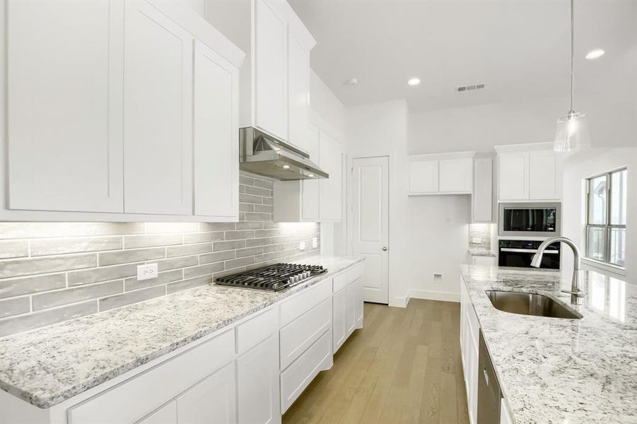 Bright kitchen featuring a gas range, stainless steel appliances, light wood-finish flooring, white cabinetry, and granite countertops