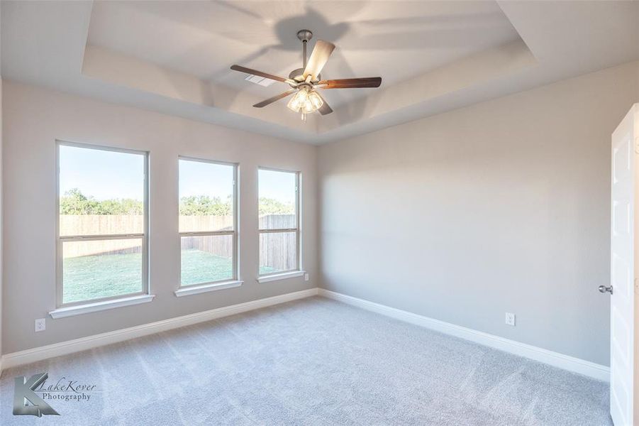 Carpeted spare room with a tray ceiling and ceiling fan