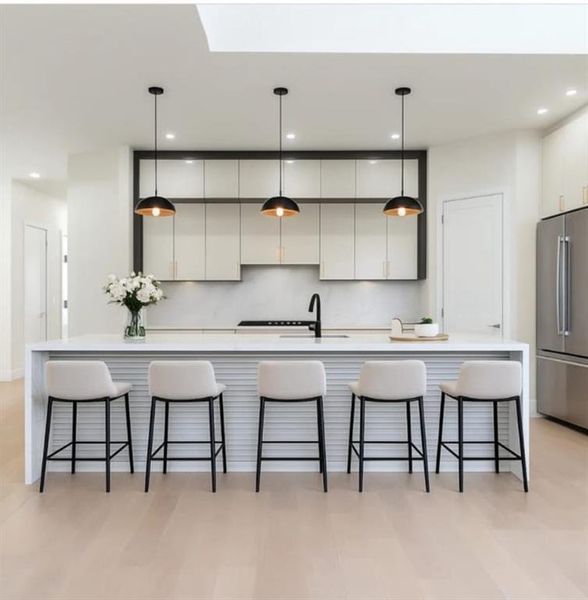 Kitchen with decorative light fixtures, freestanding refrigerator, a large island with sink, a kitchen bar, and recessed lighting