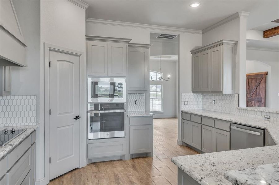 Kitchen with stainless steel appliances, backsplash, crown molding, and light hardwood / wood-style flooring