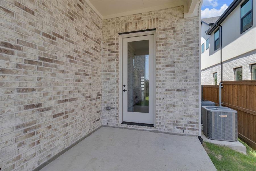 Covered patio featuring a full-light exterior door, light-toned brick facade, and concrete flooring