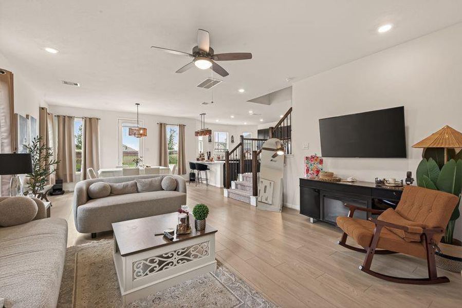 Bright open-concept living area with light wood floors, recessed lighting, and an airy staircase.
