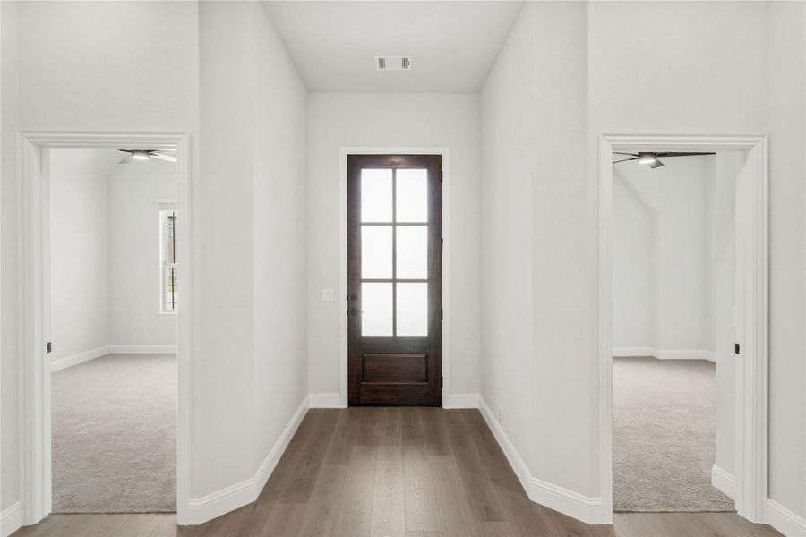 Entryway with dark wood front door, glass panels, hardwood floors, and openings to two carpeted rooms on each side. Entryway with dark wood front door, glass panels, hardwood floors, and openings to two carpeted rooms on each side.