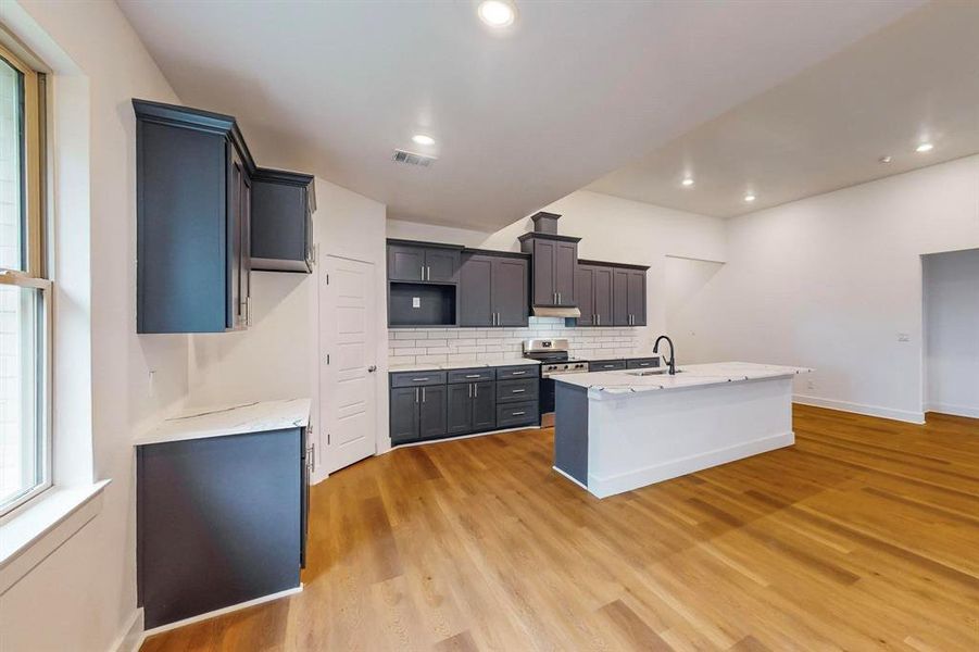 Kitchen with light hardwood / wood-style floors, decorative backsplash, sink, a kitchen island with sink, and stainless steel range