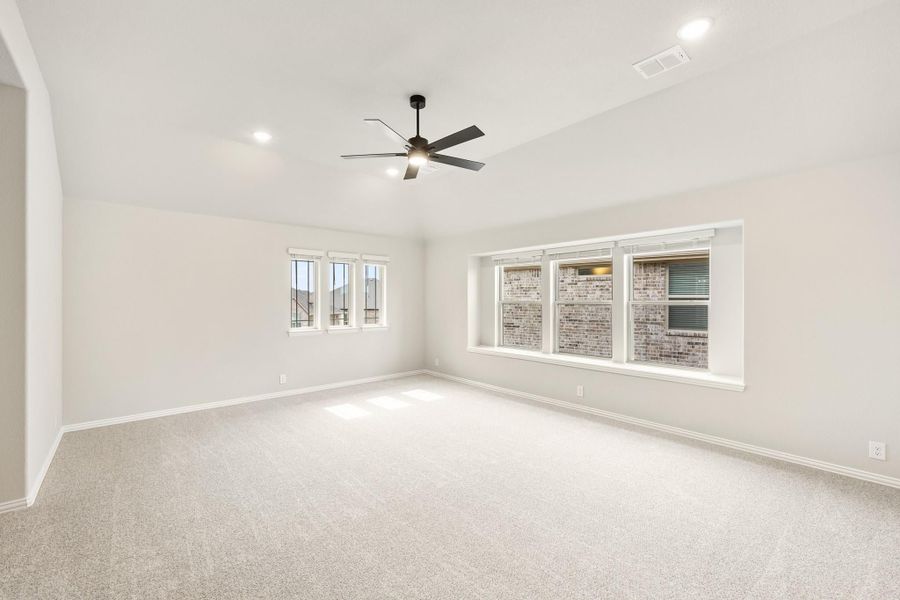 Empty room with light carpet, ceiling fan, and large windows along the back wall Empty room with light carpet, ceiling fan, and large windows along the back wall