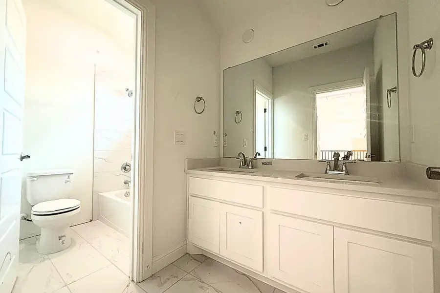 Bathroom featuring a double vanity with white cabinetry, a large frameless mirror, and a full-size bathtub with a tile surround Bathroom featuring a double vanity with white cabinetry, a large frameless mirror, and a full-size bathtub with a tile surround