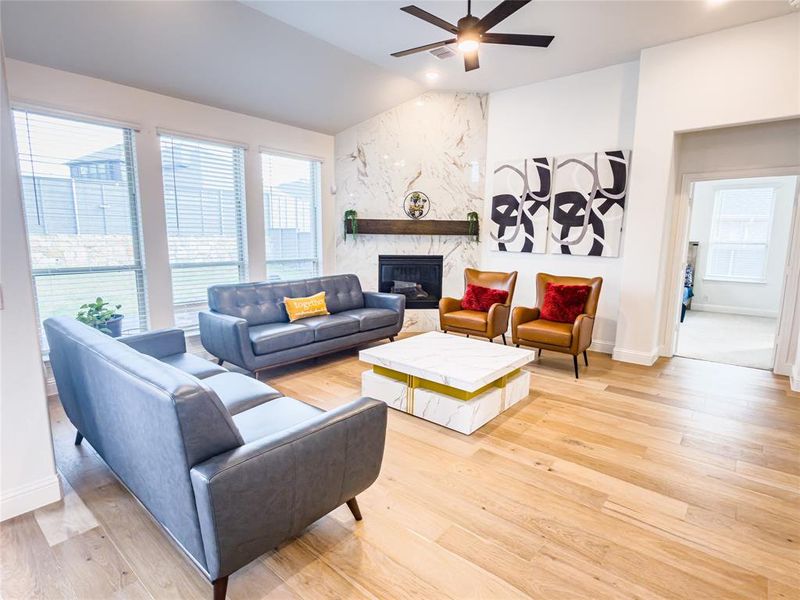 Living room with a high end fireplace, healthy amount of natural light, light wood-style floors, ceiling fan, and vaulted ceiling