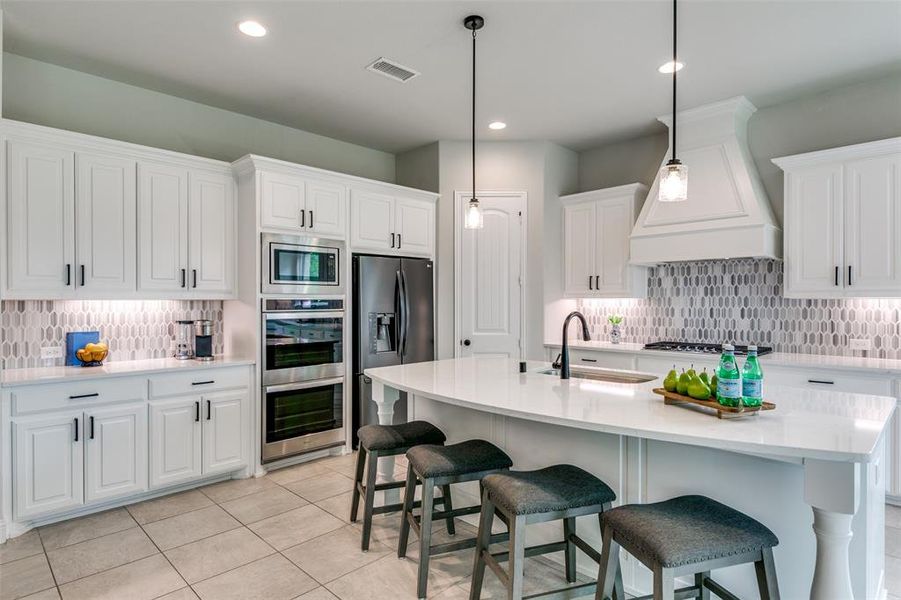 Kitchen featuring backsplash, premium range hood, appliances with stainless steel finishes, light tile floors, and pendant lighting