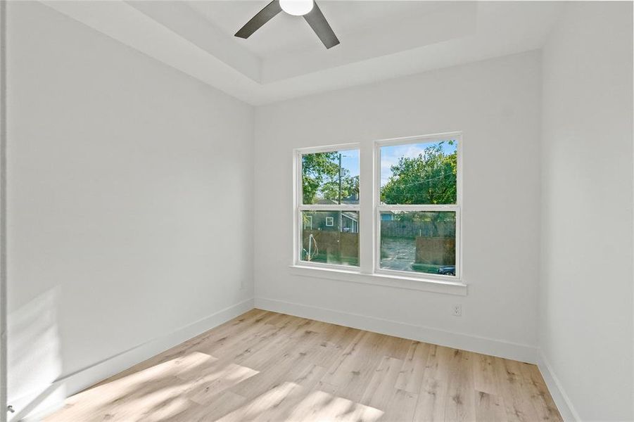 Empty room with ceiling fan, a tray ceiling, and light hardwood / wood-style floors