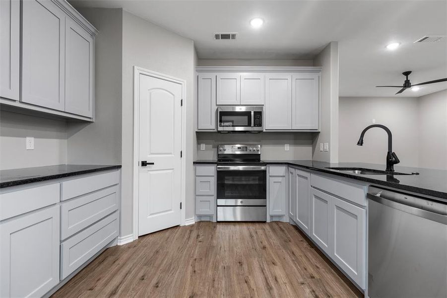 Kitchen featuring stainless steel appliances, a ceiling fan, light wood-style flooring, dark stone countertops, and recessed lighting