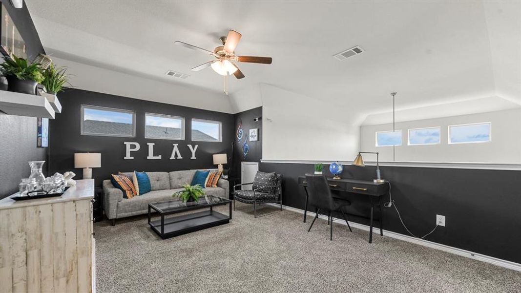 Carpeted loft space with a vaulted ceiling, ceiling fan, and multiple windows