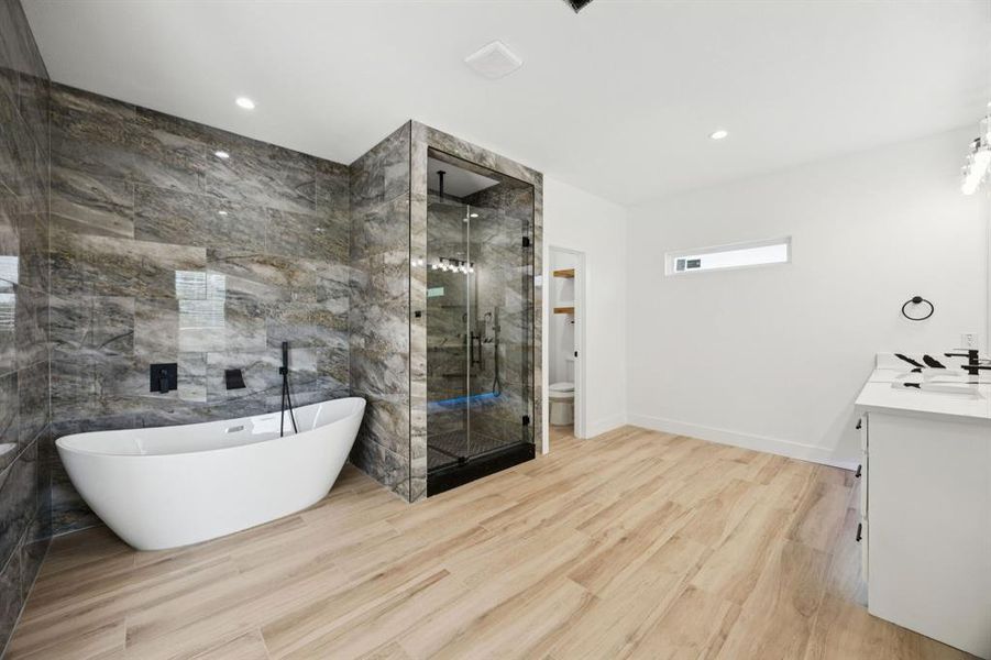 Bathroom with vanity, a shower stall, a soaking tub, tile walls, and light wood-style floors