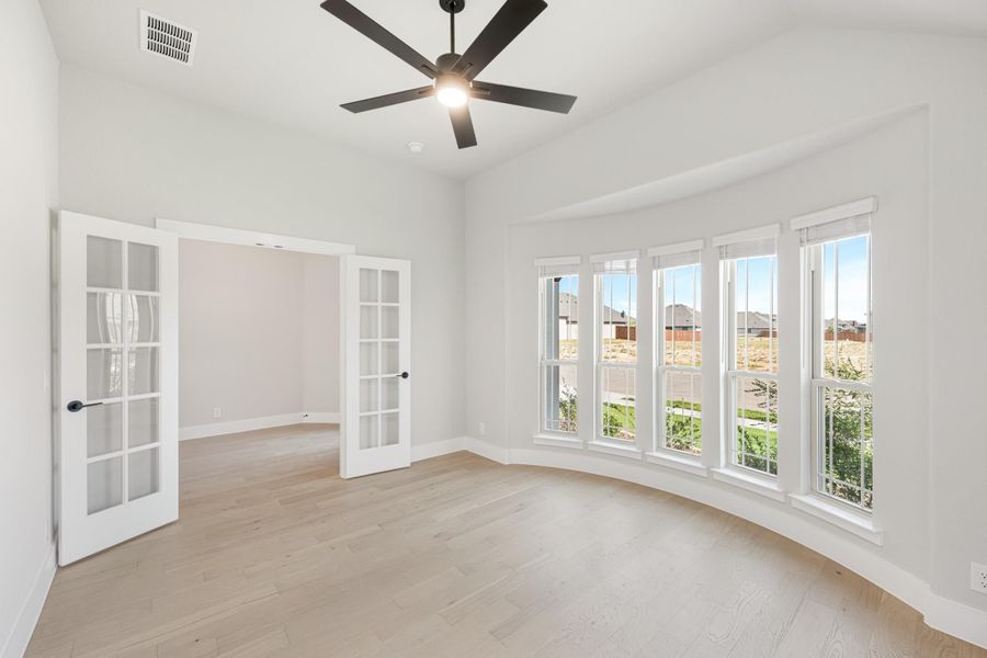 Empty room with light wood floors, French doors, large windows, and a ceiling fan Empty room with light wood floors, French doors, large windows, and a ceiling fan