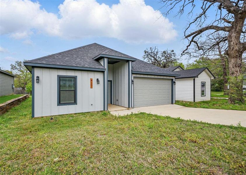 View of front of property featuring board and batten siding, a garage, roof with shingles, a front lawn, and driveway