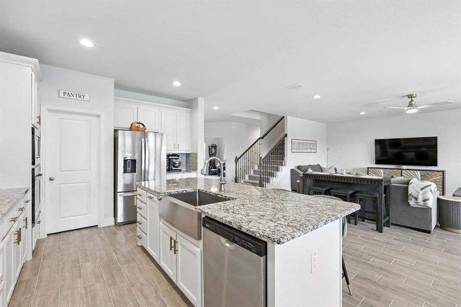 Kitchen with appliances with stainless steel finishes, ceiling fan, white cabinetry, open floor plan, and wood finish floors