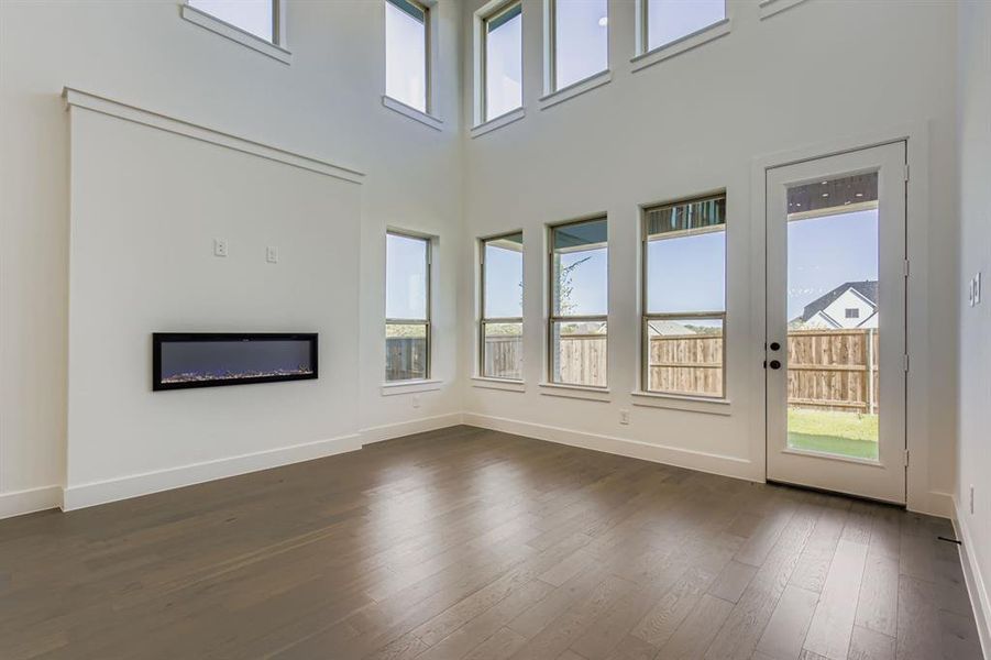 Unfurnished living room with plenty of natural light, dark wood-style flooring, a towering ceiling, and a glass covered fireplace Unfurnished living room with plenty of natural light, dark wood-style flooring, a towering ceiling, and a glass covered fireplace