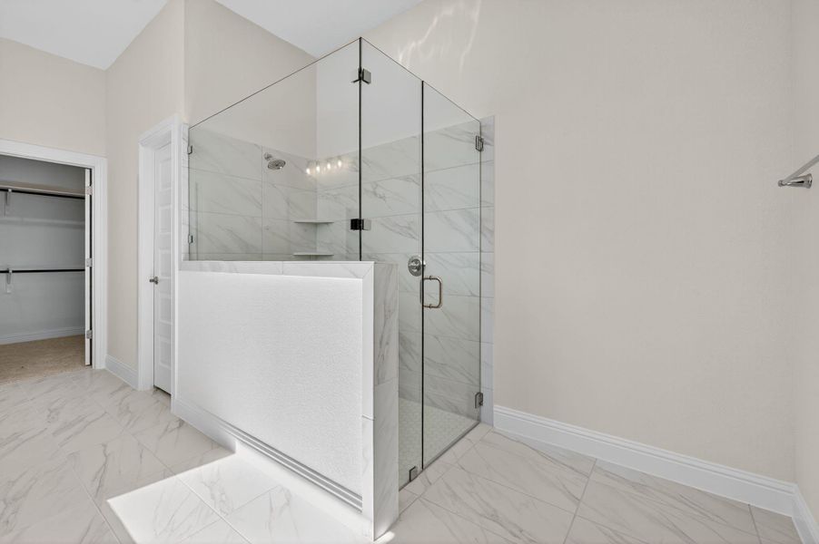 Full bathroom with a marble finish shower, a walk in closet, and light marble finish floors
