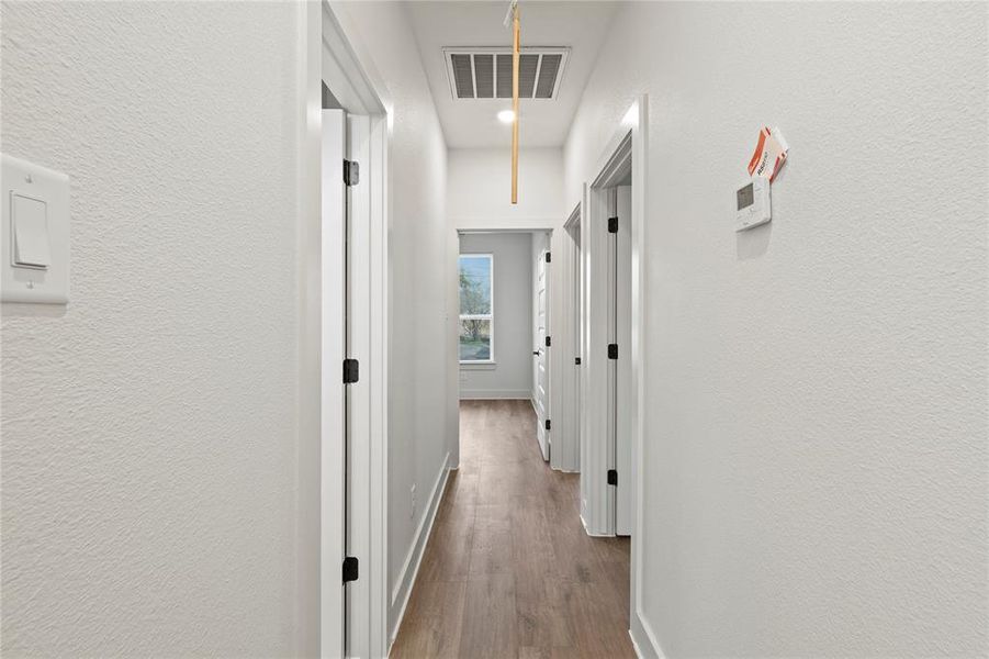 Hall with a textured wall, wood finished floors, visible vents, baseboards, and attic access