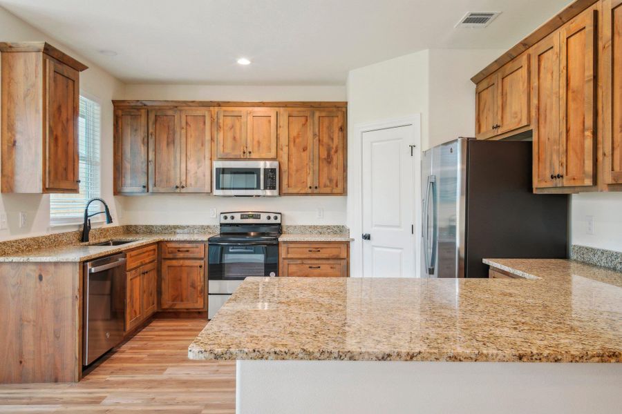 Kitchen with visible vents, light stone countertops, a peninsula, stainless steel appliances, and a sink